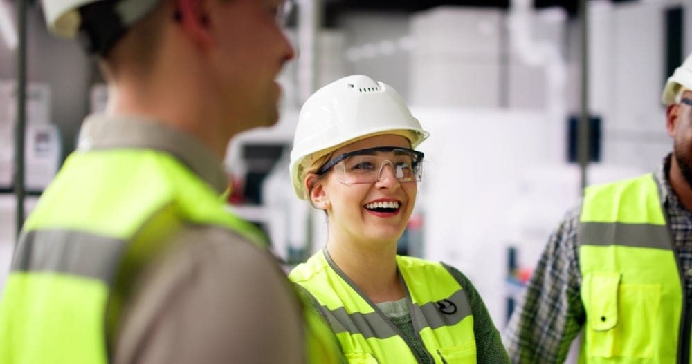 Skilled trades plant workers in reflective safety gear are engaged in cheerful conversation.